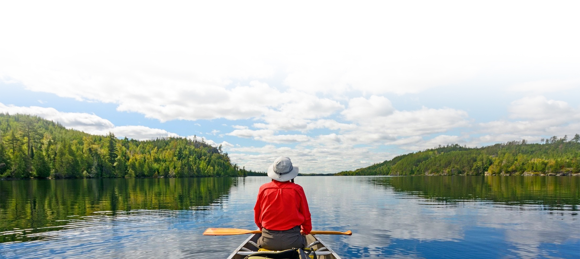 A woman is canoeing on a calm lake on a beautiful summer sunny day
