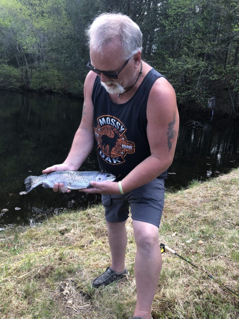 A Man Holding a Live Fish Infront of a Pond